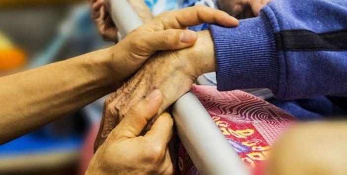 mani di un anziano che stringono altre mani