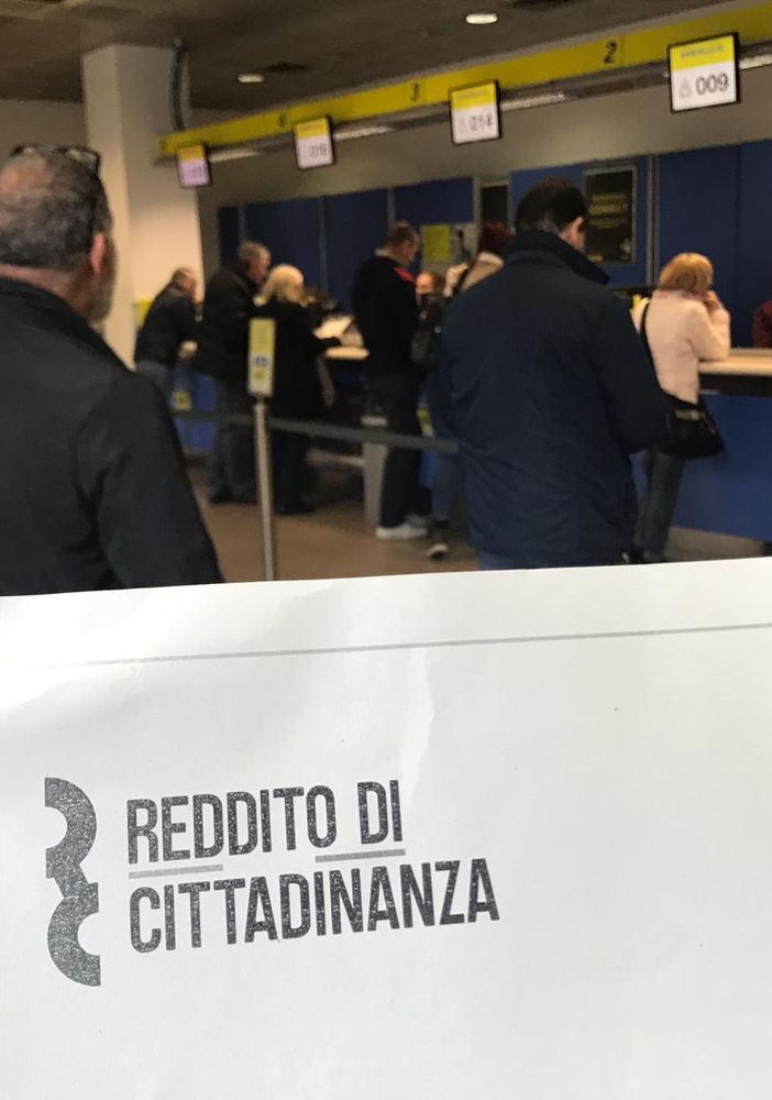 Persone in coda, mentre un cartello in primo piano riporta la scritta "reddito di cittadinanza" Persone in coda, mentre un cartello in primo piano riporta la scritta "reddito di cittadinanza"
